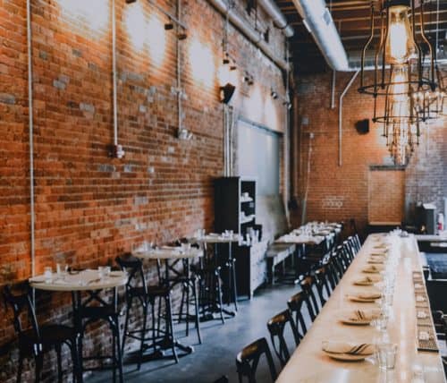 interior designer restaurant bar marble countertop orange brick wall place settings brown chairs black wire light fixtures
