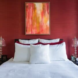 interior design bedroom red wallpaper accent wall yellow gold pink abstract art white bedspread LK Design