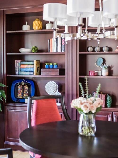 interior design family room library built-in shelves art collection round table red chair flowers