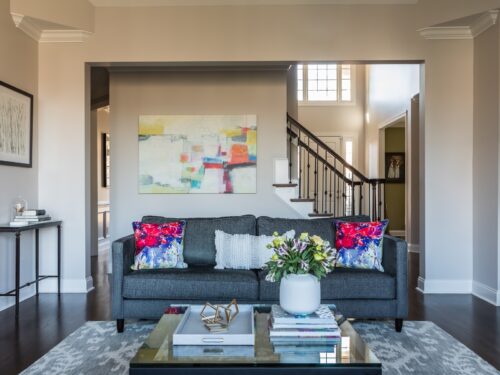 interior design living room abstract art gray sofa couch colorful throw pillows patterned rug glass coffee table