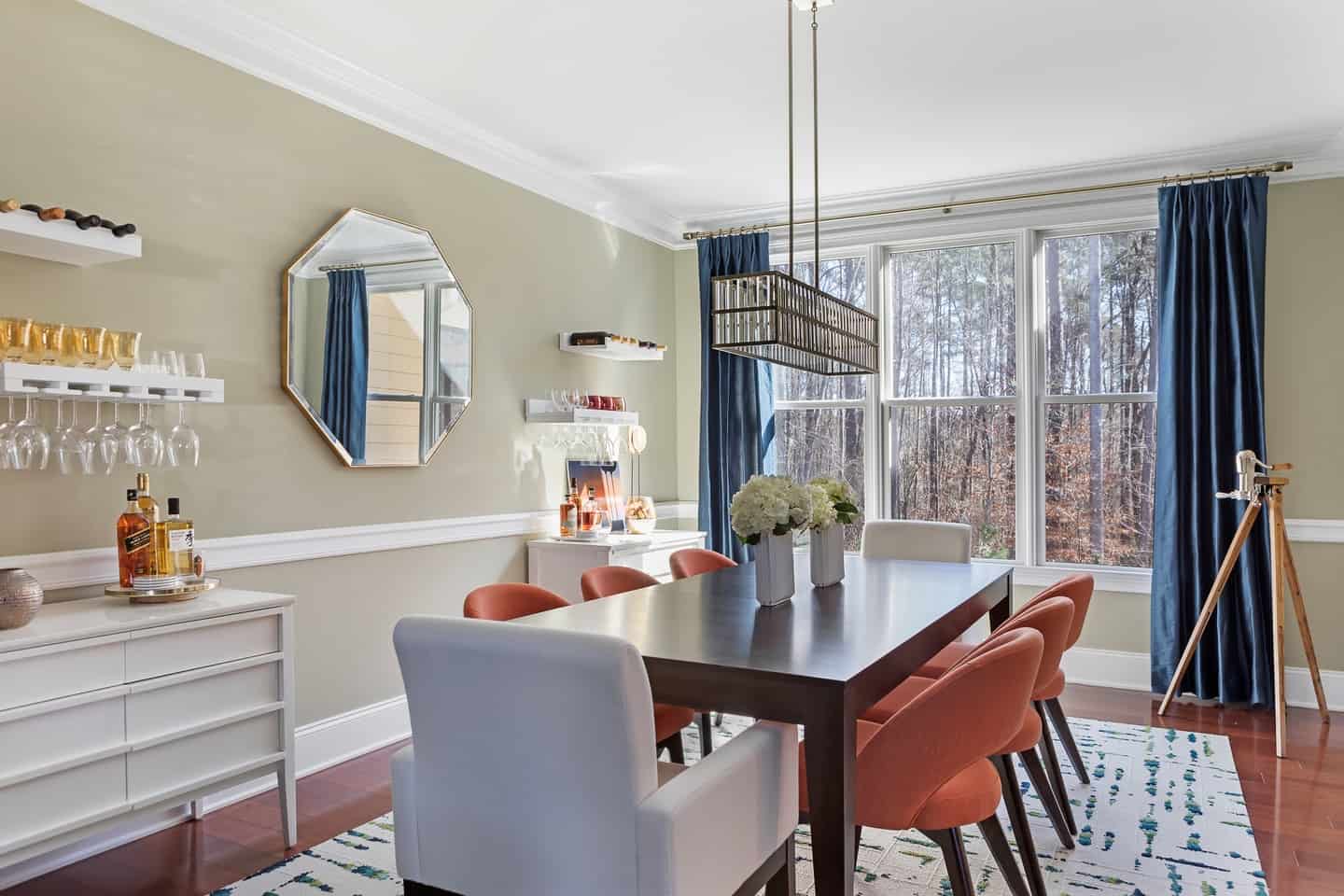 interior designer modern dining room black table orange chairs octagon mirror statement chandelier floral arrangement