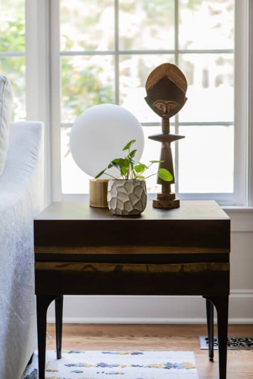 brown wood end table by the window potted plant globe lamp tribal figurine by LK interior design