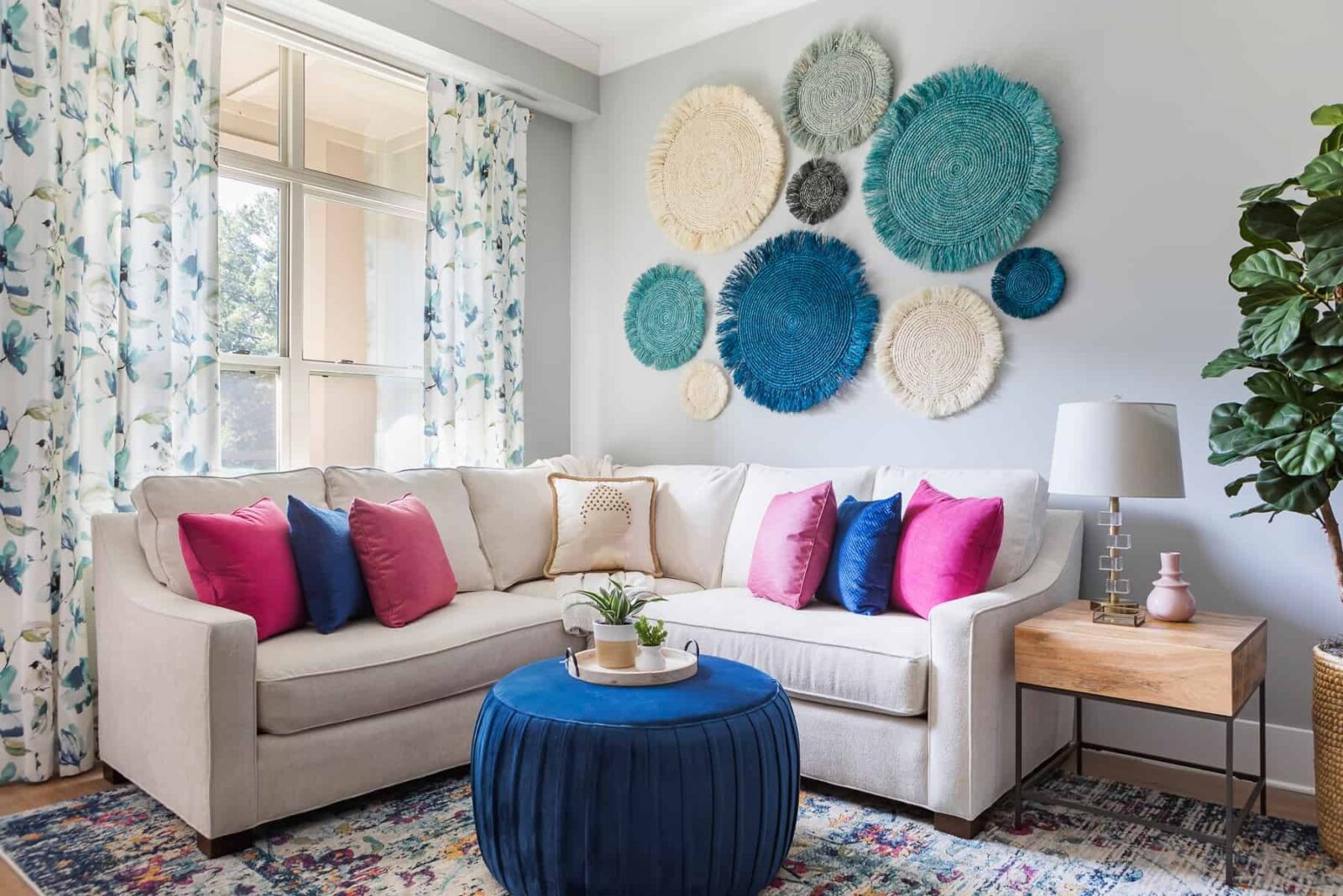 family room white sectional sofa with colorful pillows blue ottoman colorful rug draperies curtains seagrass art