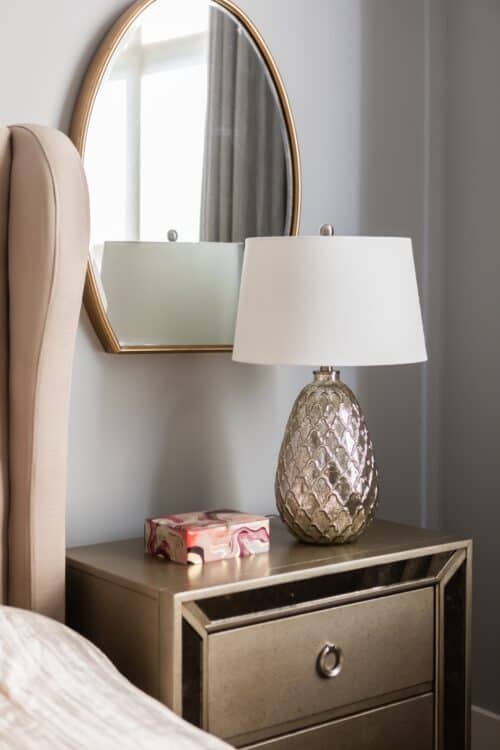 bedroom night stand gold champagne accents lamp oval mirror gray walls light pink accents
