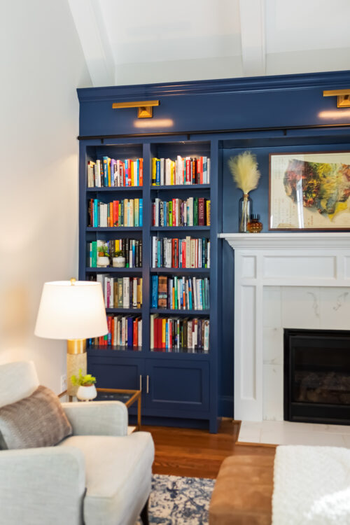 LK Design Home library blue shelves with ladder white fireplace beige armchair lamp ottoman pillows custom