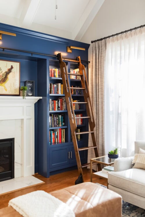 LK Design Home library blue shelves with ladder white fireplace beige armchair lamp ottoman pillows custom window treatments curtains
