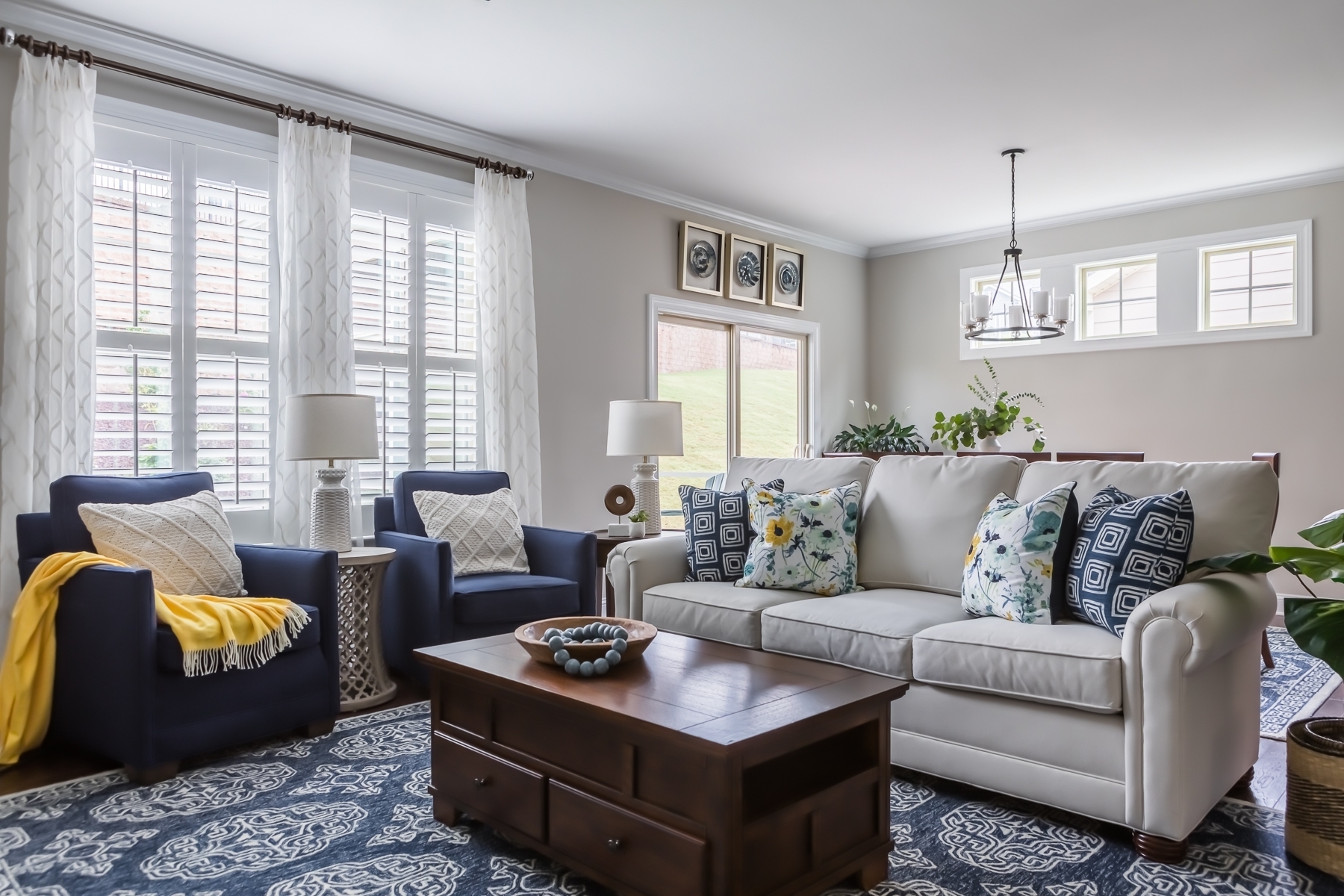A traditional blue and white living room look: solid color furniture in neutral and deep blue accented by the bright and bold patterns of the accent pillows, patterned rug